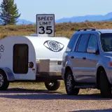 Srebrny SUV z przyczepą kempingową "Little Guy" pod znakiem ograniczenia prędkości do 35. Czy mając C+E można jeździć B+E? Tak, uprawnienia C+E obejmują B+E.