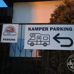 Znak "KAMPER PARKING" z ikoną kampera i strzałką w lewo. Obok znak "PARKING" z logo restauracji i hotelu.