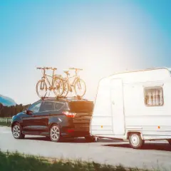 Czarny SUV z rowerami na dachu i przyczepa kempingowa na drodze. Idealne miejsce, gdzie można parkować przyczepy kempingowe, to malownicze tereny z widokiem na góry.