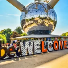 Bruksela nietypowe miejsca: Atomium wita turystów napisem "WELCOME". Słońce odbija się w stalowej kuli, a ludzie spacerują wokół.
