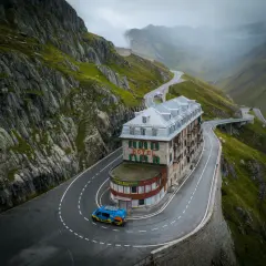 Kamper na serpentynach w drodze do Szwajcarii, obok zabytkowego hotelu Belvedere. Górzysty krajobraz, mgła w oddali.
