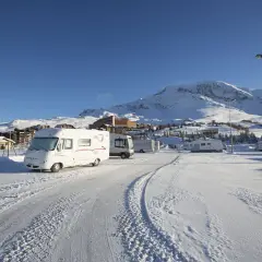 Zimowy parking w Alpe d'Huez, pełen kamperów, pod ośnieżonymi szczytami.
