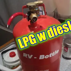Czerwona butla gazowa RV-Bottle z zaworem, gotowa do tankowania LPG w dieslu. Obok puszka kawy Illy.