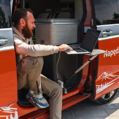 Mężczyzna pracuje na laptopie przy otwartych drzwiach kampera. Idealne miejsce na podróż kamperem, by połączyć pracę z przygodą.