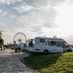 Darmowe parkingi Łeba: kamienista droga, kampery, samochody i diabelski młyn w tle.