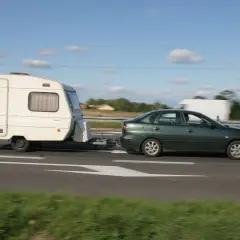 Zielony samochód ciągnie przyczepę kempingową. Ważne jest, jak obliczyć DMC zespołu pojazdów, by podróżować bezpiecznie.