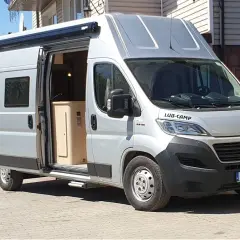 Srebrny kamper Ducato L3H3, z otwartymi drzwiami, ukazuje wnętrze. Idealny do podróży, jego wymiary pozwalają na komfort.