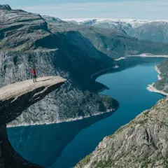 Osoba z rękami w górze na Trolltungę, słynnej skale w Norwegii, z widokiem na jezioro i góry.