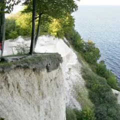 Kobieta na skraju urwiska podziwia klify nad Bałtykiem. Wokół bujna zieleń i szum fal.