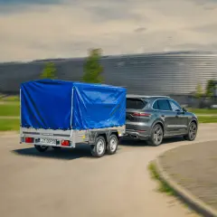 Szare Porsche Cayenne z niebieską plandeką na przyczepie dwuosiowej. Czy można ciągnąć przyczepę dwuosiową na kat. B?