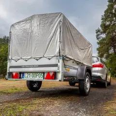 Samochód z przyczepą na leśnej drodze. Warto wiedzieć, jak cofac z przyczepą, by bezpiecznie dotrzeć do celu.
