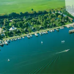 Widok z lotu ptaka na camping marina PTTK z licznymi łodziami i żaglówkami zacumowanymi przy brzegu, otoczony zielenią i polami.