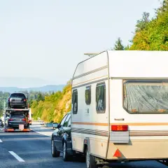 Samochód ciągnie przyczepę kempingową. Na autostradzie widać też inne pojazdy, w tym lawetę z samochodami. Winieta co to? To opłata za przejazd.