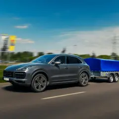Szary SUV z przyczepą pod niebieską plandeką toczy się po autostradzie.