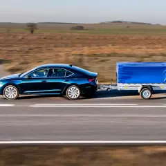 Ciemnoniebieski sedan ciągnie przyczepę z niebieską plandeką. Może to być sytuacja, gdy dmc przyczepy większe niż w dowodzie, ale wygląda na stabilną.