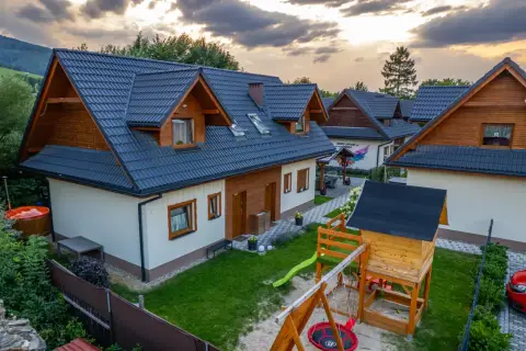 Piękne brenna widoki z domkami i placem zabaw. W oddali góry, a na niebie chmury.