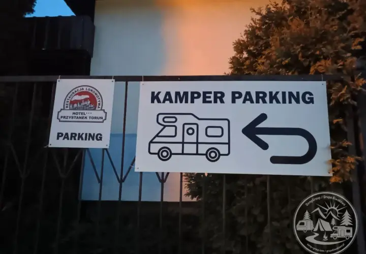Znak "KAMPER PARKING" z ikoną kampera i strzałką w lewo. Obok znak "PARKING" z logo restauracji i hotelu.