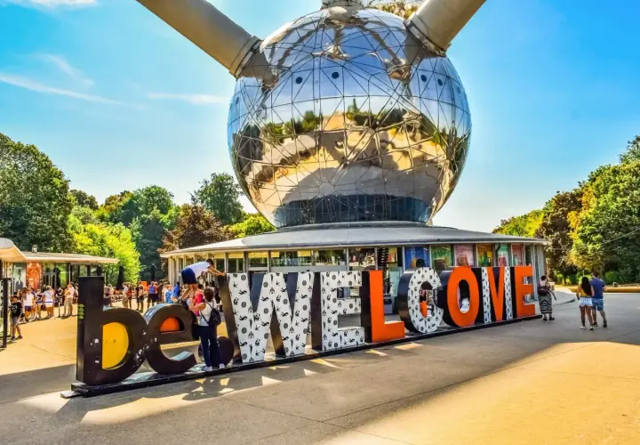 Bruksela nietypowe miejsca: Atomium wita turystów napisem "WELCOME". Słońce odbija się w stalowej kuli, a ludzie spacerują wokół.