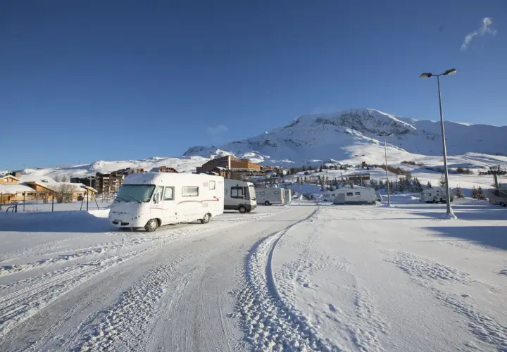 Zimowy parking w Alpe d'Huez, pełen kamperów, pod ośnieżonymi szczytami.