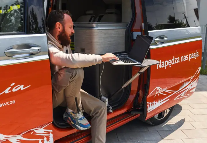 Mężczyzna pracuje na laptopie przy otwartych drzwiach kampera. Idealne miejsce na podróż kamperem, by połączyć pracę z przygodą.
