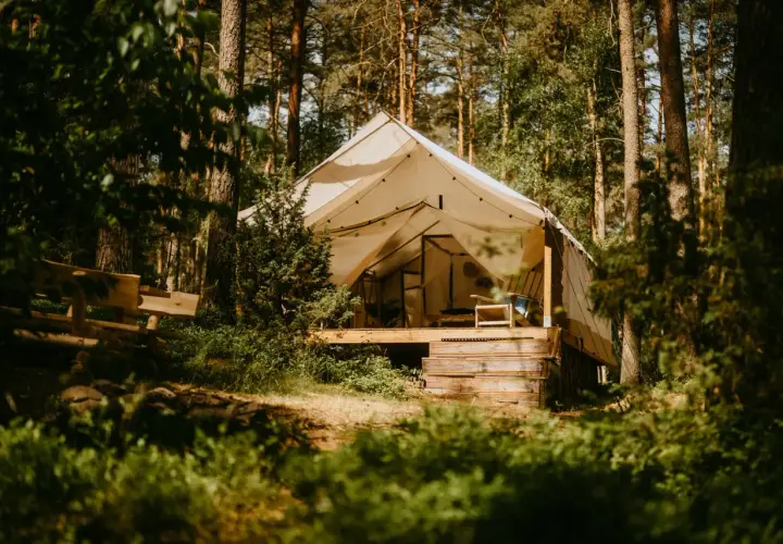 Namiot glampingowy w lesie, idealny na darmowe pola namiotowe Mazury. Drewniana ławka i krzesło zapraszają do odpoczynku.
