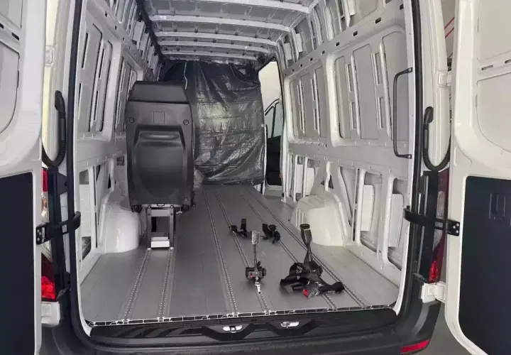 Wnętrze białego vana, przygotowywanego jako pojazd specjalny kempingowy. Widoczne szyny montażowe, fotel i plandeka. Przepisy dotyczące adaptacji są kluczowe.