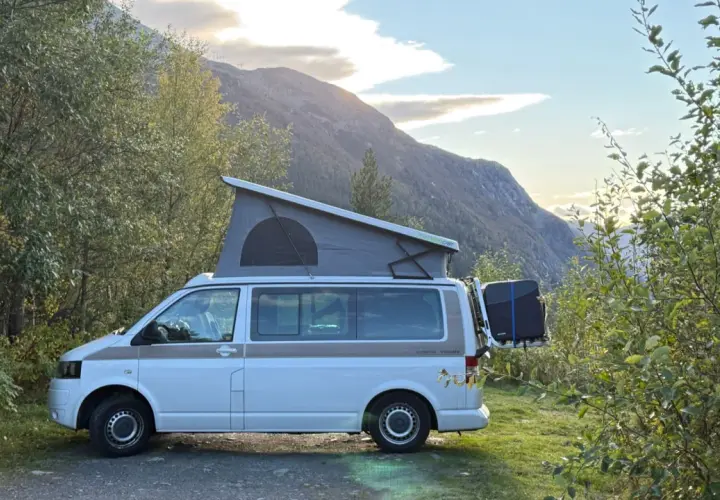 Kamper z podnoszonym dachem zaparkowany przy drodze w górach. Piękny widok na norweskie krajobrazy, idealne na podróż po **autostrady w Norwegii**.