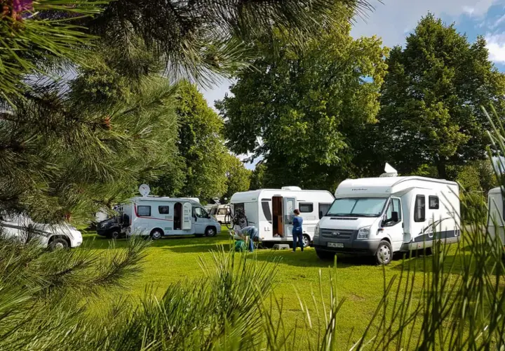 Kampery i przyczepy kempingowe na zielonej trawie, wśród drzew. Słoneczny dzień w **nude camp**.