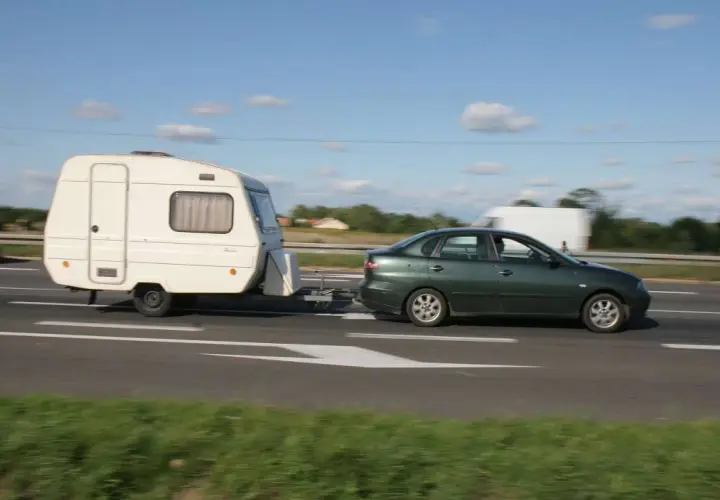Zielony samochód ciągnie przyczepę kempingową. Ważne jest, jak obliczyć DMC zespołu pojazdów, by podróżować bezpiecznie.