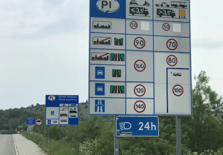Znaki drogowe informujące o opłatach i ograniczeniach prędkości na drodze dwujezdniowej.