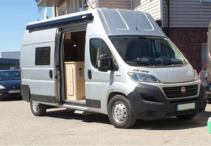Srebrny kamper Ducato L3H3, z otwartymi drzwiami, ukazuje wnętrze. Idealny do podróży, jego wymiary pozwalają na komfort.