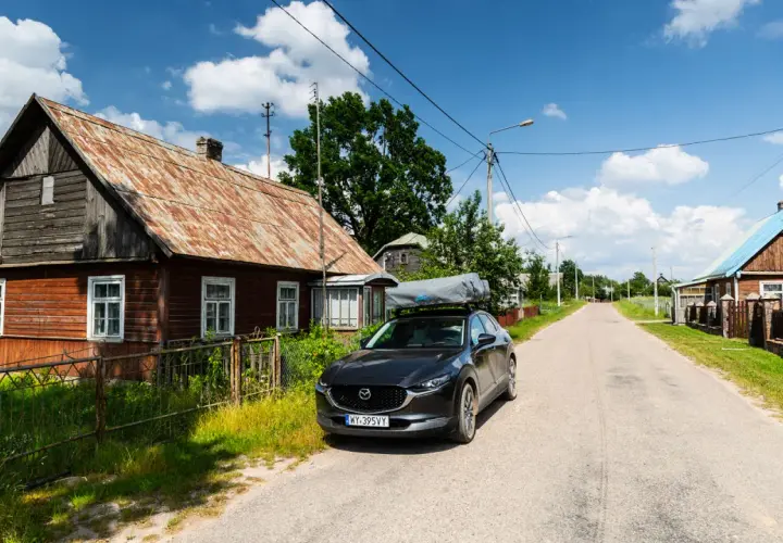 Czarny SUV z namiotem dachowym zaparkowany przy drewnianym domu, w drodze wzdłuż wschodniej granicy.