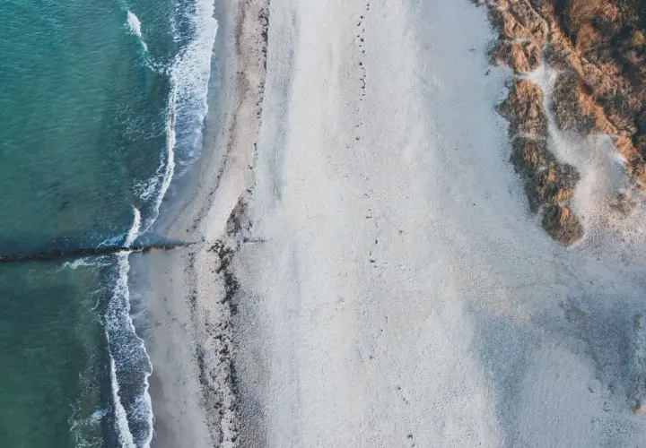 Puste plaże nad morzem, gdzie fale delikatnie muskają piasek, a wydmy porośnięte trawą tworzą naturalną granicę.