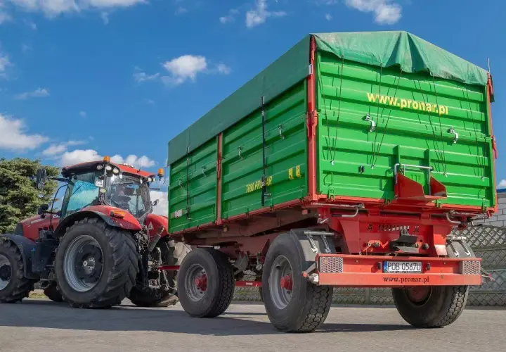 Czerwony traktor z zieloną przyczepą. Dowiedz się, jakich przyczep nie trzeba rejestrować, by sprawnie pracować w polu.