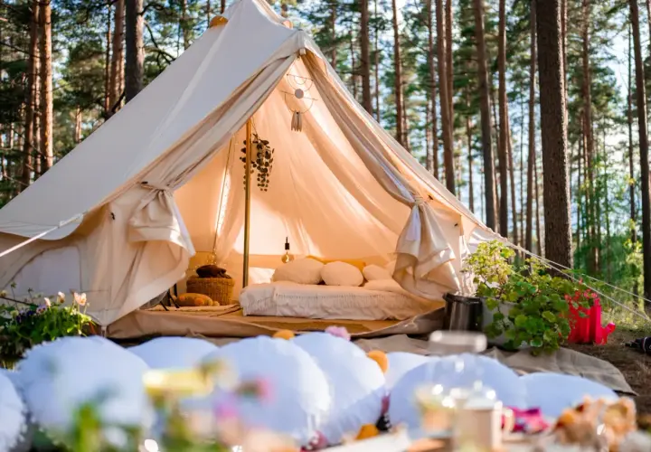 Wygodny namiot w lesie, z łóżkiem i dekoracjami, to właśnie glamping co to jest – luksusowy kemping.
