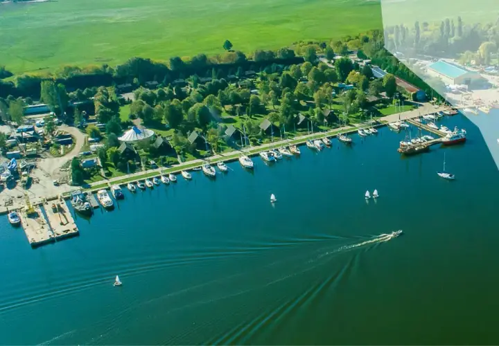 Widok z lotu ptaka na camping marina PTTK z licznymi łodziami i żaglówkami zacumowanymi przy brzegu, otoczony zielenią i polami.