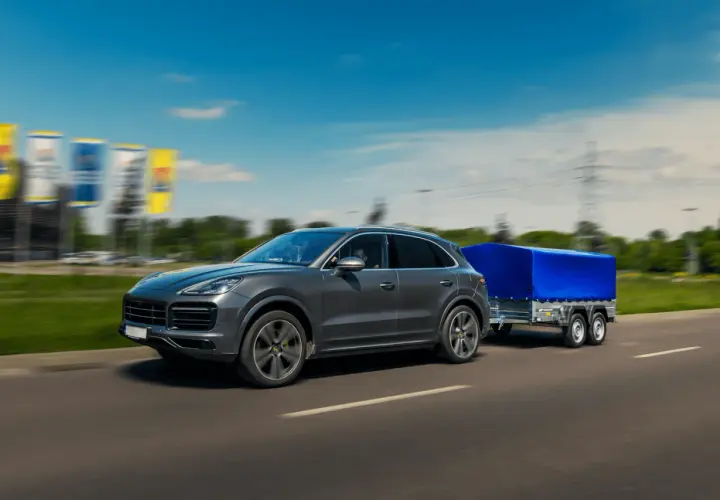Szary SUV z przyczepą pod niebieską plandeką toczy się po autostradzie.