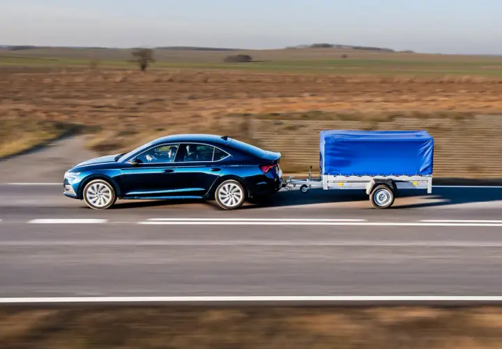 Ciemnoniebieski sedan ciągnie przyczepę z niebieską plandeką. Może to być sytuacja, gdy dmc przyczepy większe niż w dowodzie, ale wygląda na stabilną.