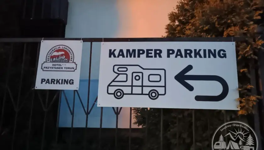 Znak "KAMPER PARKING" z ikoną kampera i strzałką w lewo. Obok znak "PARKING" z logo restauracji i hotelu.