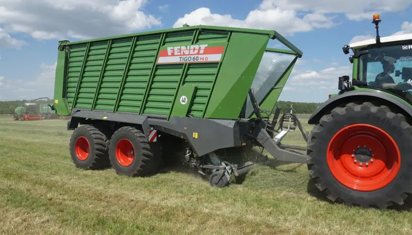 Zielona przyczepa Fendt Tigo 60 PR D, maszyna rolnicza, której kraj pochodzenia to Niemcy, pracuje na polu.