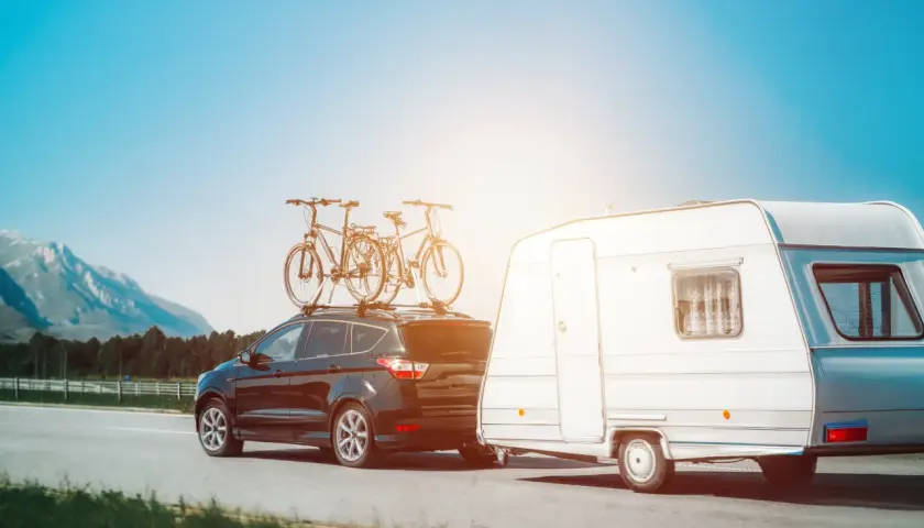 Czarny SUV z rowerami na dachu i przyczepa kempingowa na drodze. Idealne miejsce, gdzie można parkować przyczepy kempingowe, to malownicze tereny z widokiem na góry.