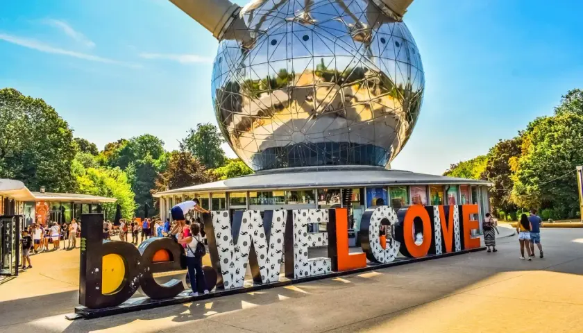 Bruksela nietypowe miejsca: Atomium wita turystów napisem "WELCOME". Słońce odbija się w stalowej kuli, a ludzie spacerują wokół.
