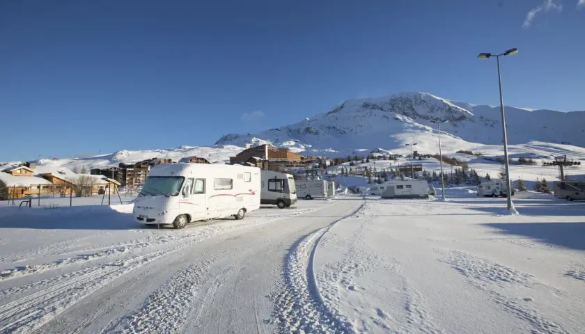 Zimowy parking w Alpe d'Huez, pełen kamperów, pod ośnieżonymi szczytami.