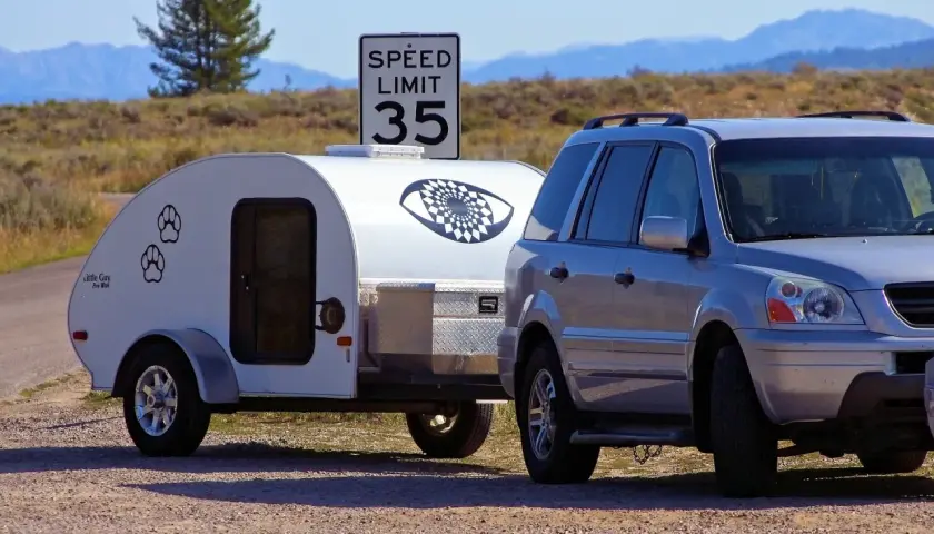 Srebrny SUV z przyczepą kempingową "Little Guy" pod znakiem ograniczenia prędkości do 35. Czy mając C+E można jeździć B+E? Tak, uprawnienia C+E obejmują B+E.