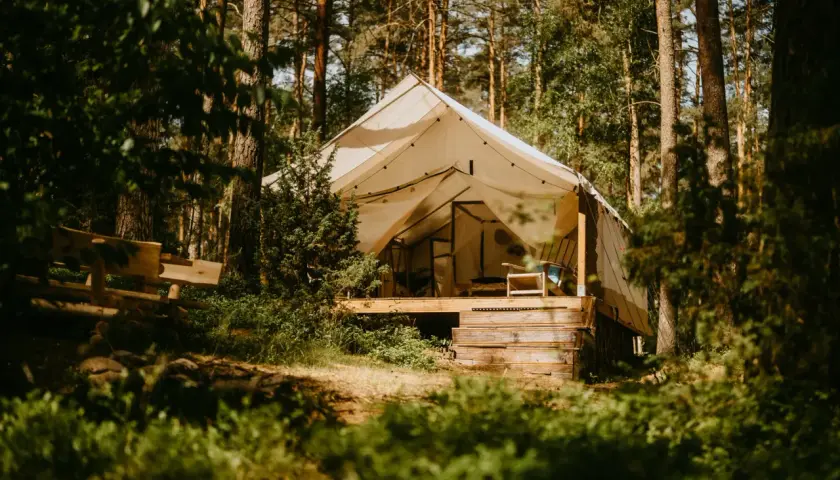 Namiot glampingowy w lesie, idealny na darmowe pola namiotowe Mazury. Drewniana ławka i krzesło zapraszają do odpoczynku.