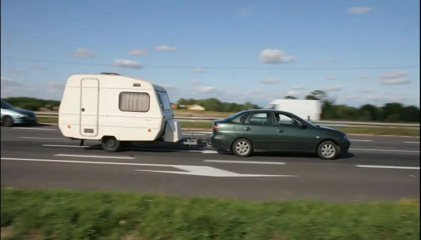Zielony samochód ciągnie przyczepę kempingową. Ważne jest, jak obliczyć DMC zespołu pojazdów, by podróżować bezpiecznie.