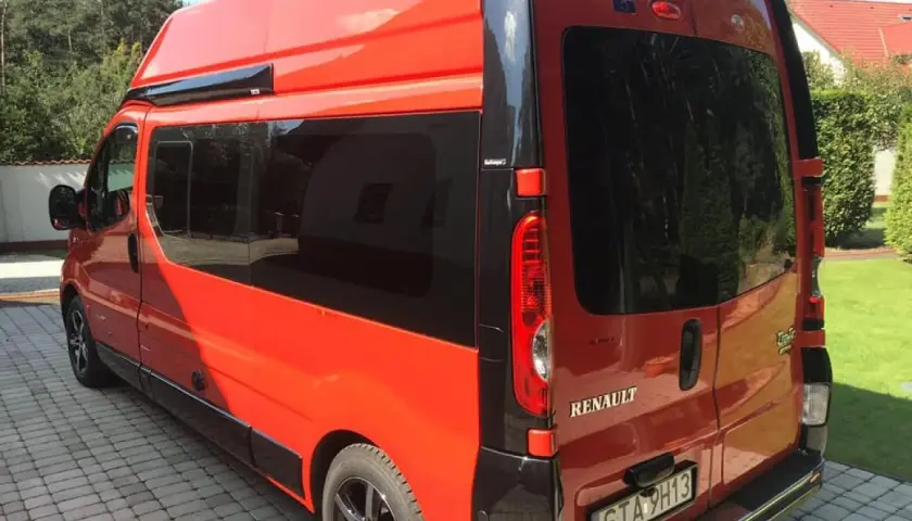 Pomarańczowy Renault Trafic L2H2 z przyciemnianymi szybami stoi na podjeździe z kostki brukowej.