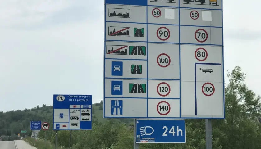 Znaki drogowe informujące o opłatach i ograniczeniach prędkości na drodze dwujezdniowej.