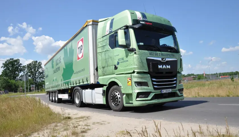 Zielona ciężarówka MAN z naczepą TIP na drodze. Długość zestawu c+e robi wrażenie, idealna do transportu.