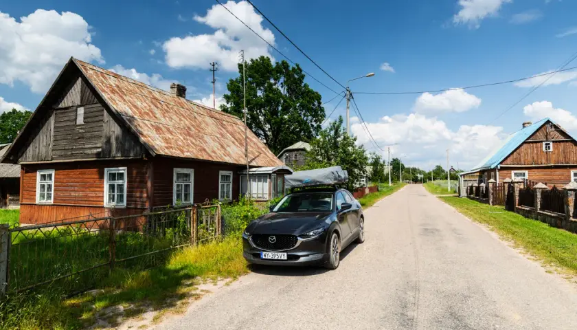 Czarny SUV z namiotem dachowym zaparkowany przy drewnianym domu, w drodze wzdłuż wschodniej granicy.